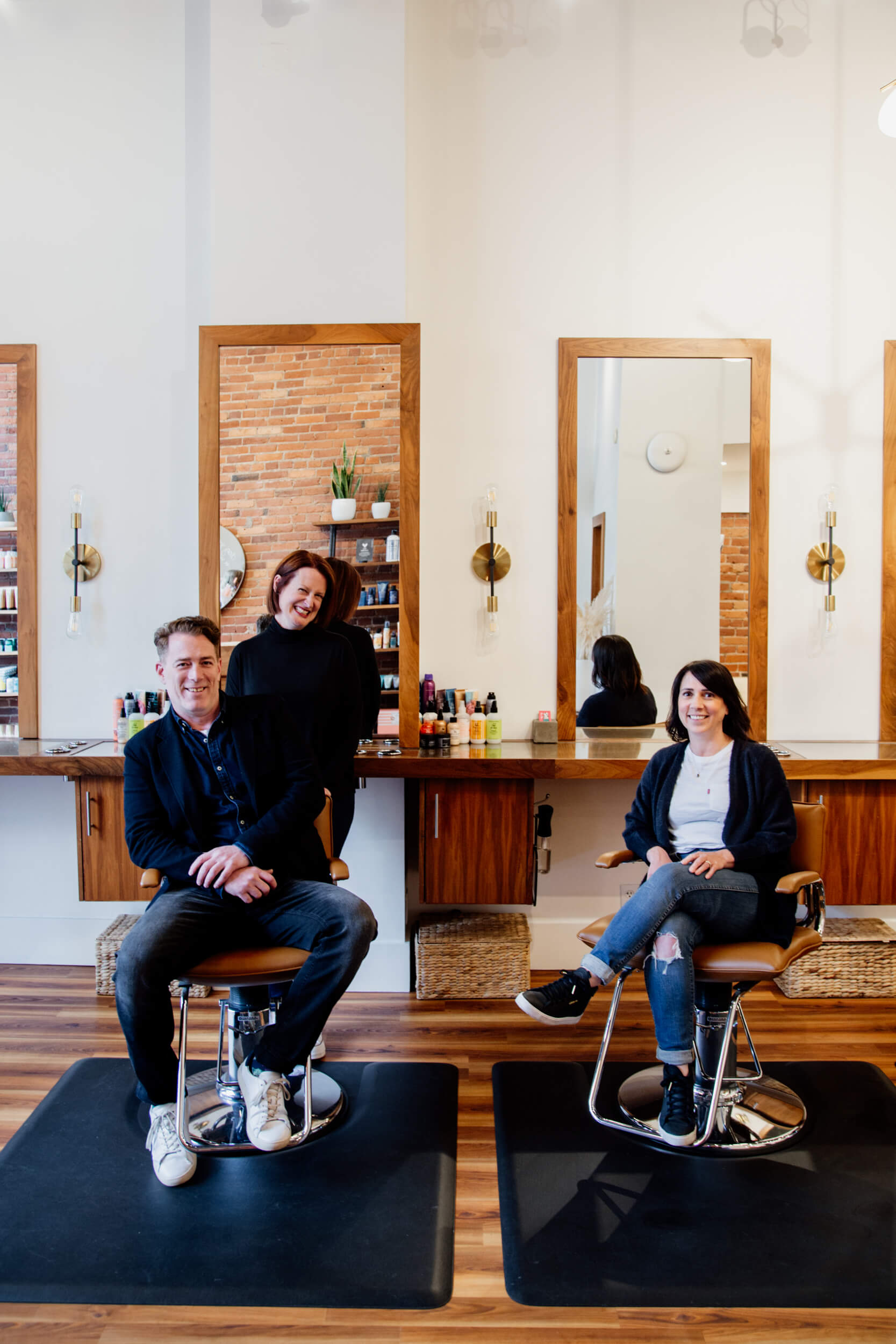 Three salon owners smile at camera while sitting on chairs.