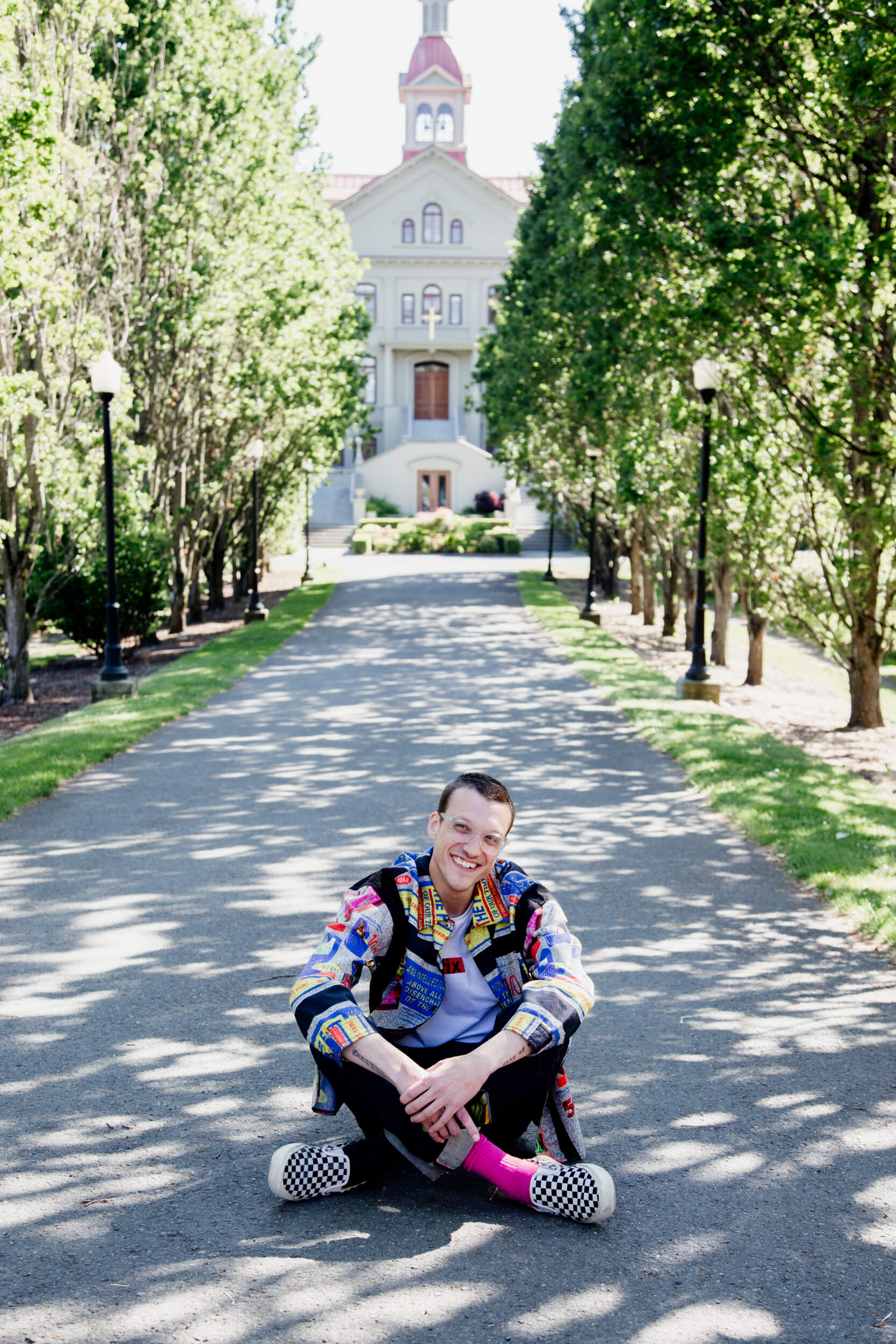 Man sitting on pathway in front of a building surrounded by trees.