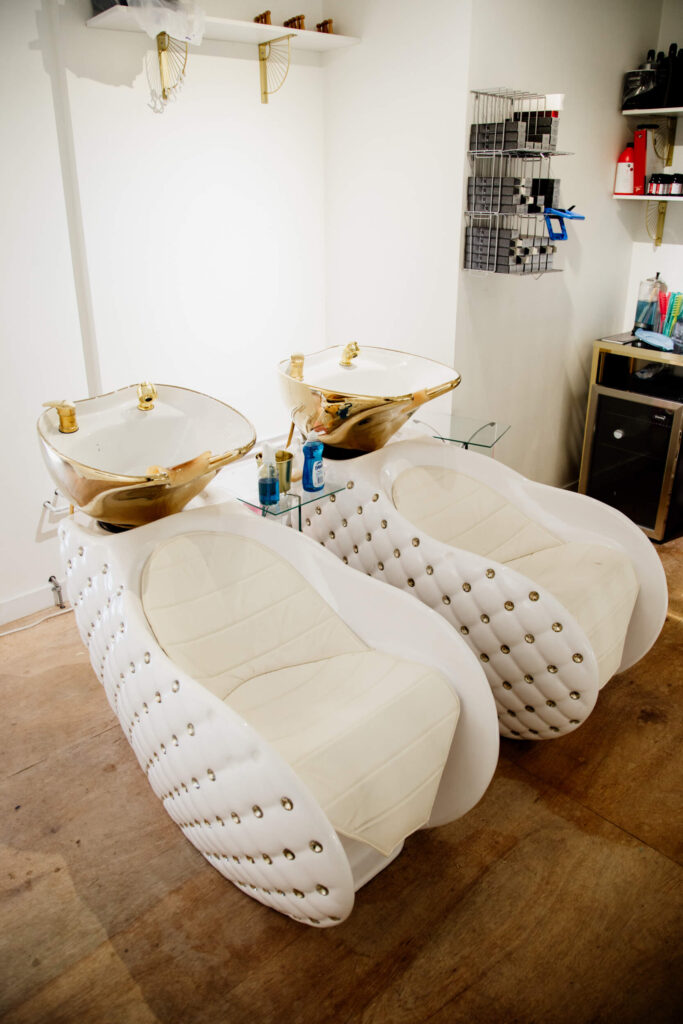 Two white and gold hair washing chairs in a salon.