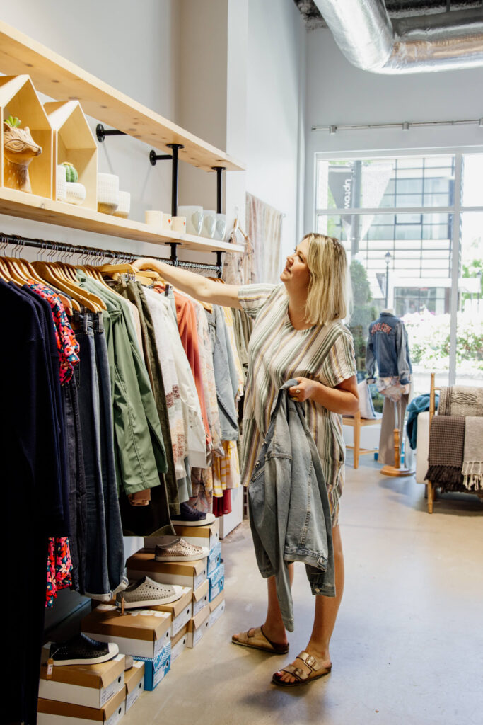 A  shop owner organizes clothing on the racks in her store in Victoria, BC.