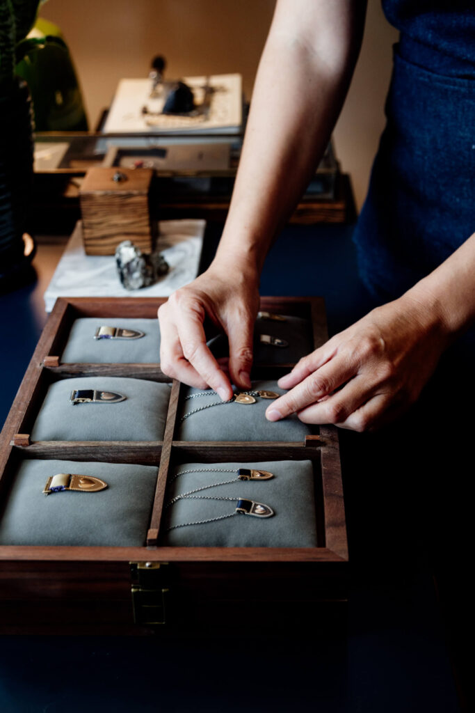 A pair of hands arranges some metal jewellery in a satin box.