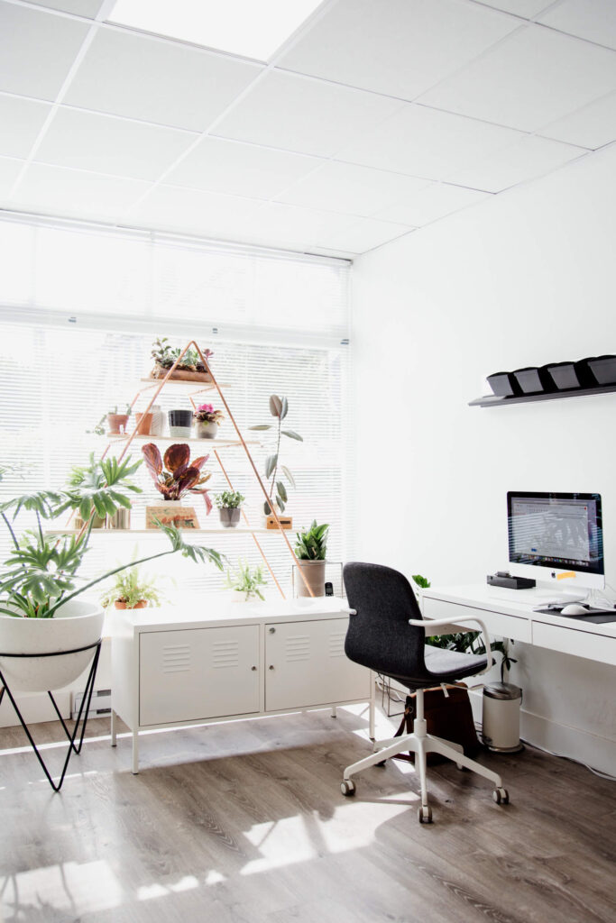 An office chair and desk by a window with plants.