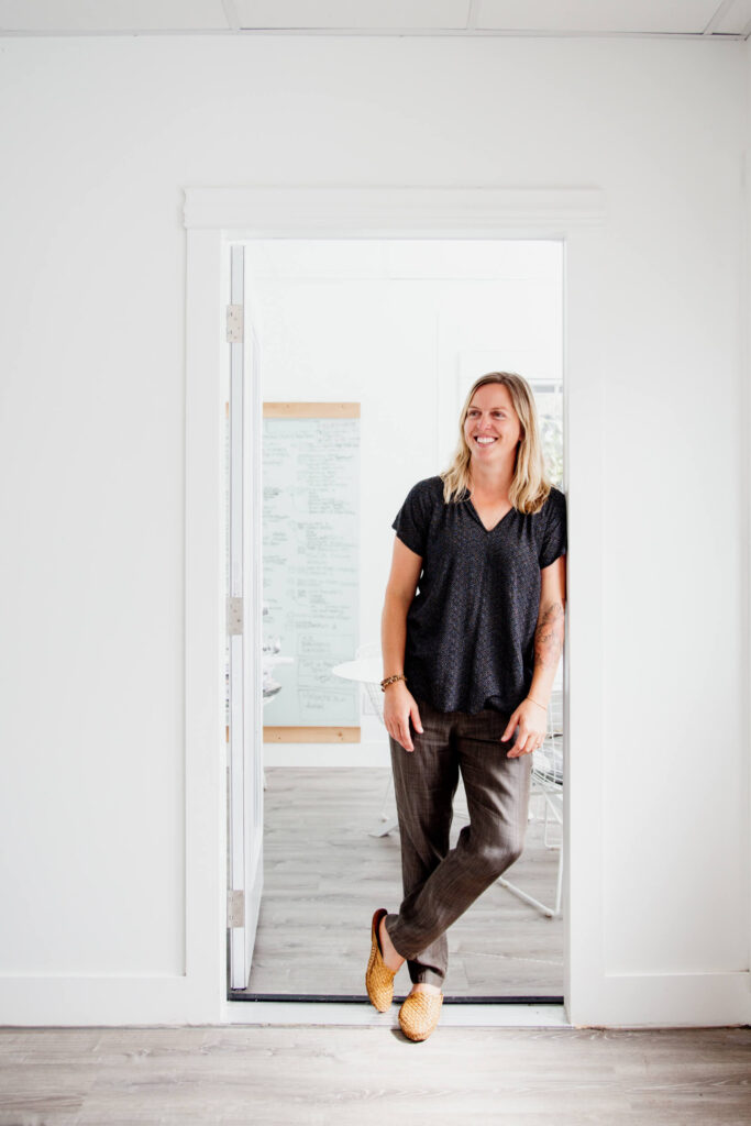 a woman leans against a door frame and smiles.