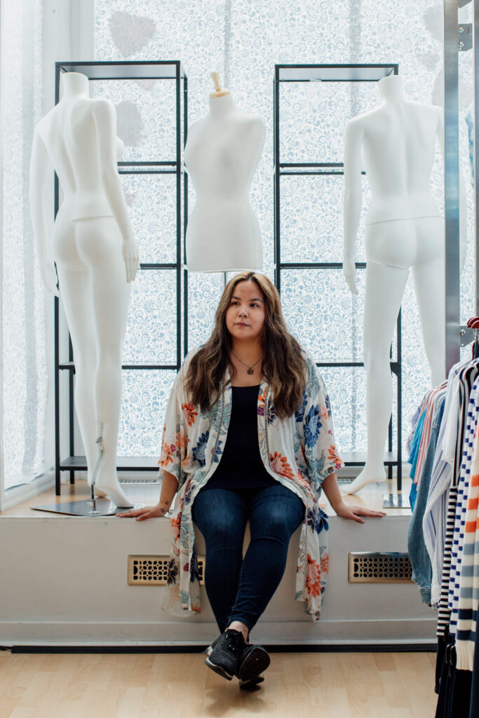 A shop owner sits in her shop window looking thoughtful.