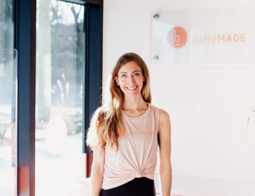 The owner of a barre studio stands and smiles at her desk in Victoria, BC.