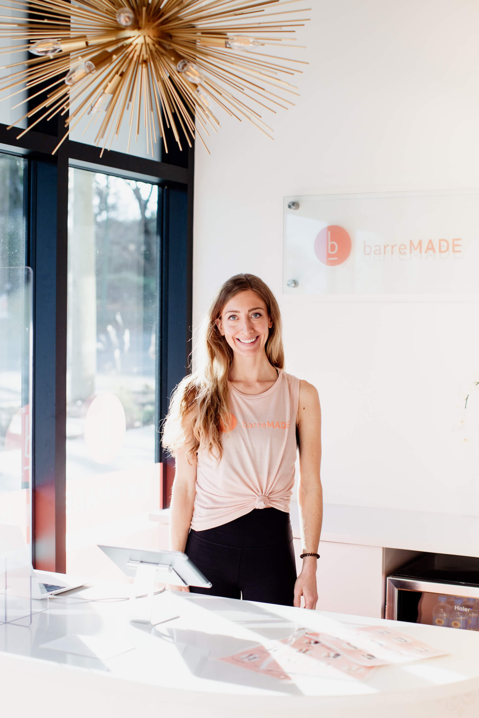 The owner of a barre studio stands and smiles at her desk in Victoria, BC.