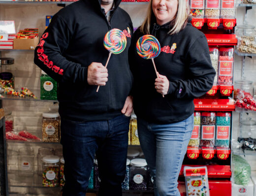 A couple stands in front of their candy shelf.