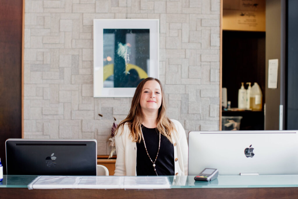 A woman smiles behind the desk in her yoga studio.